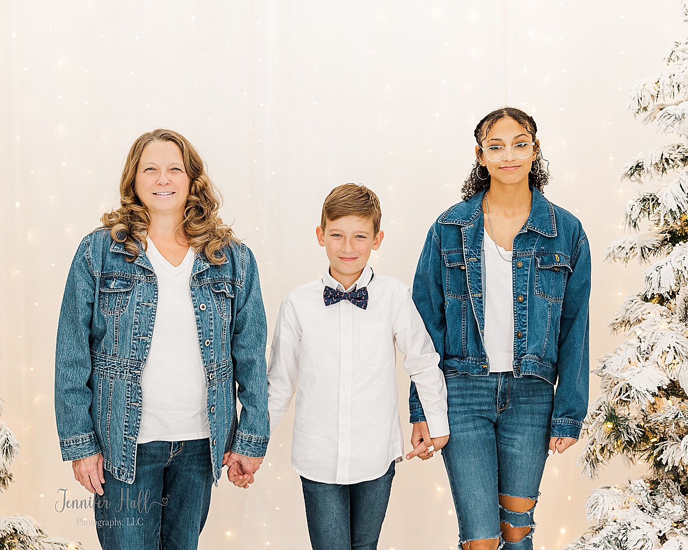 Family standing together and holding hands by Christmas trees indoors for Christmas family portraits in a North East, PA, portrait studio.