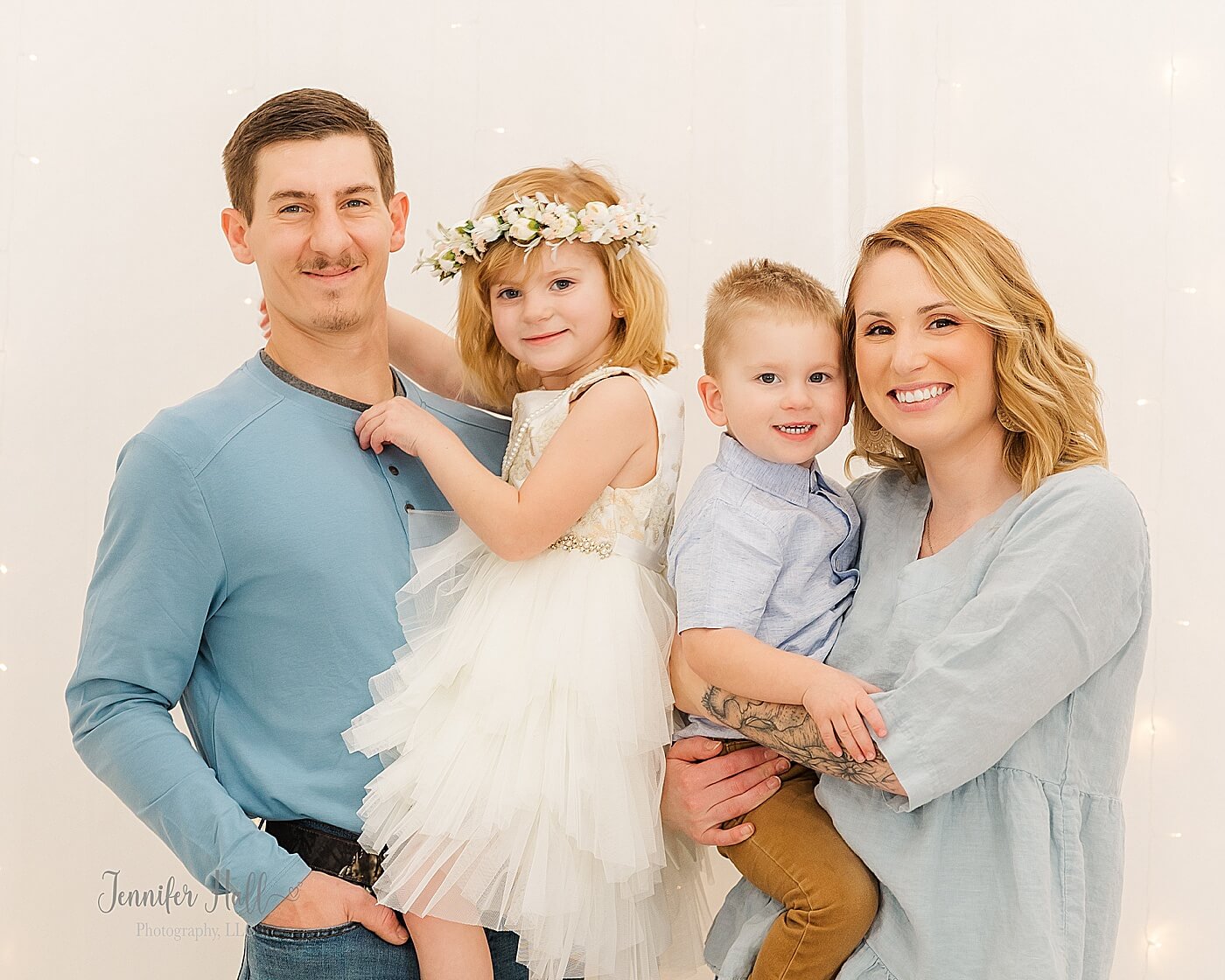 Family with blue outfits standing close together in front of a light wall for family studio Easter photography near Erie, PA.