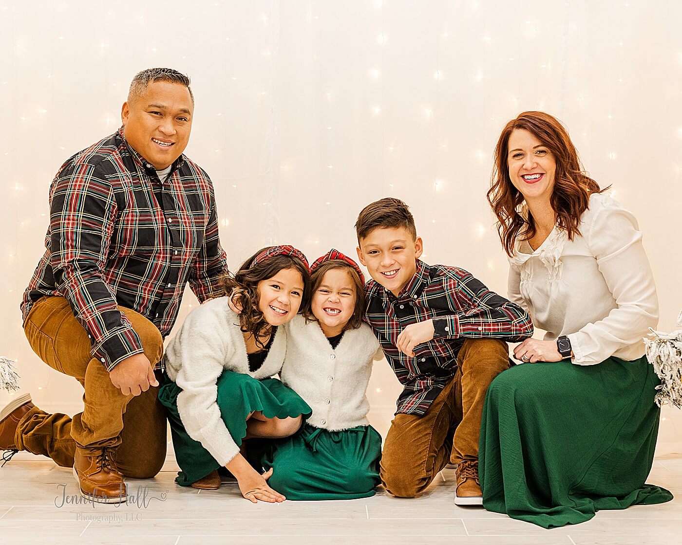 Family kneeling in front of a light wall by Christmas trees for a Christmas studio family portrait session near Erie, PA.