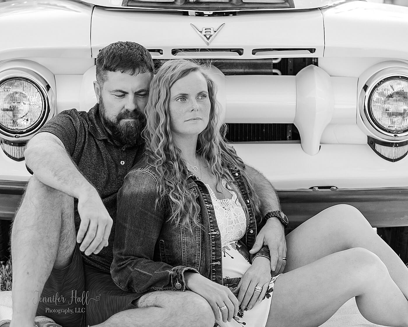 Mother and father sitting in front of a white Ford truck outdoors for summer family photos with a vintage truck near Erie, PA.