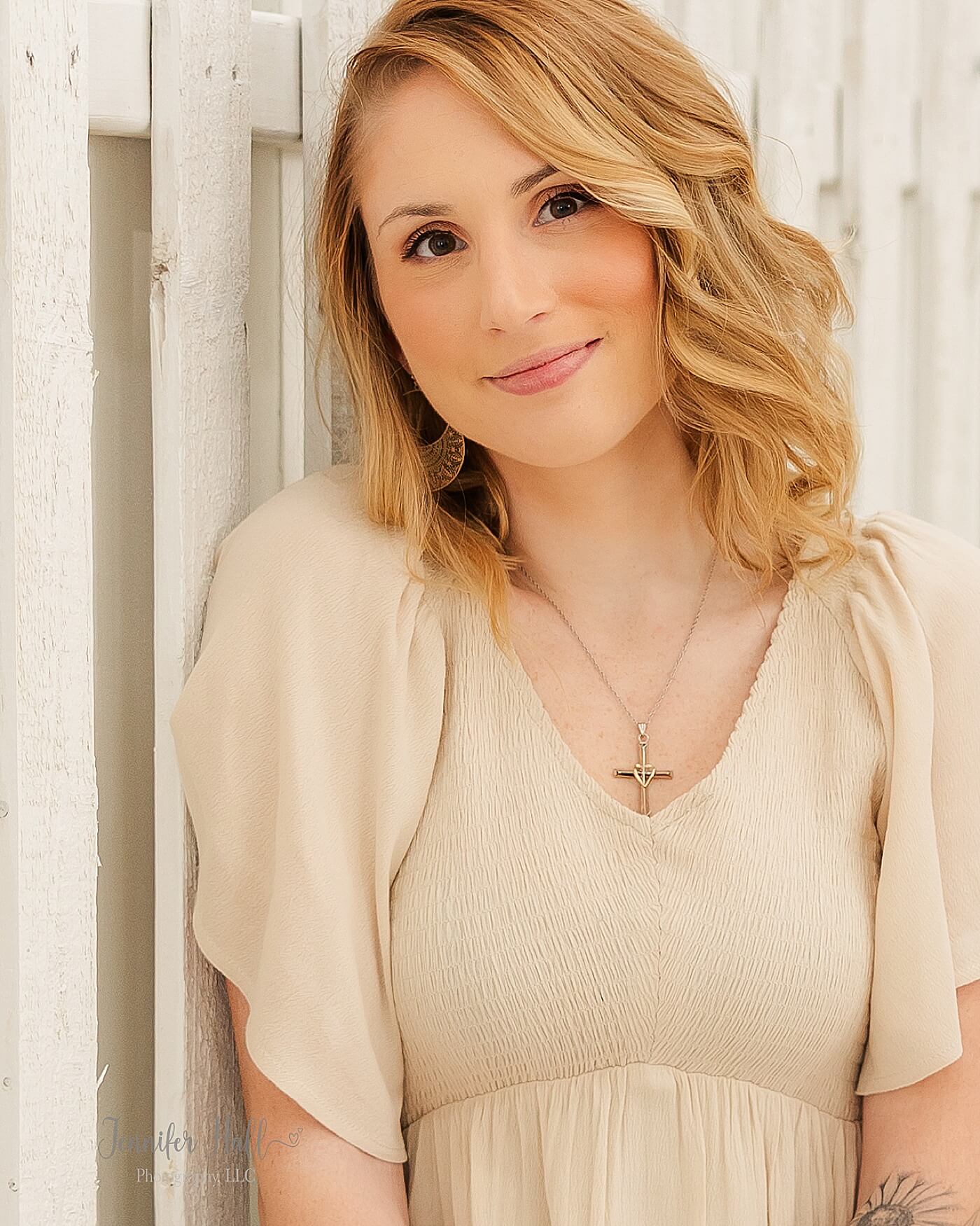 Woman with a beige dress by a white fence in an indoor studio to show styling tips for her for what to wear for a family portrait session.