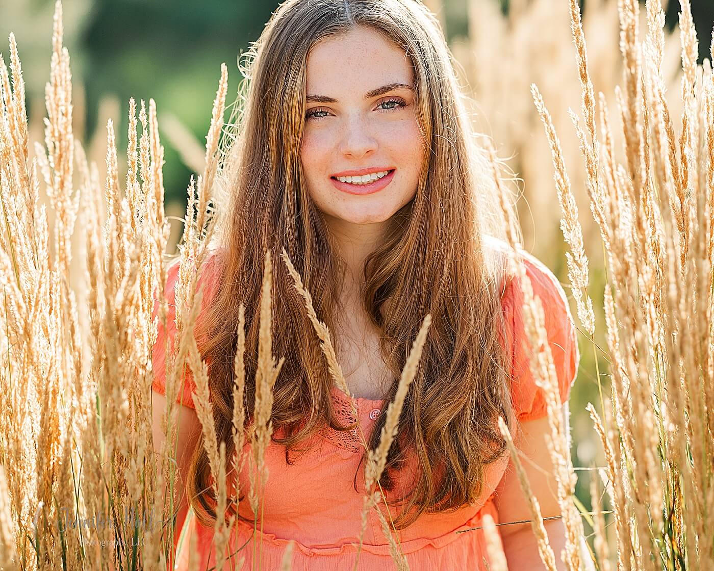 Girl with a coral shirt standing outdoors in beige, ornamental grass for summer senior photos in North East, PA.