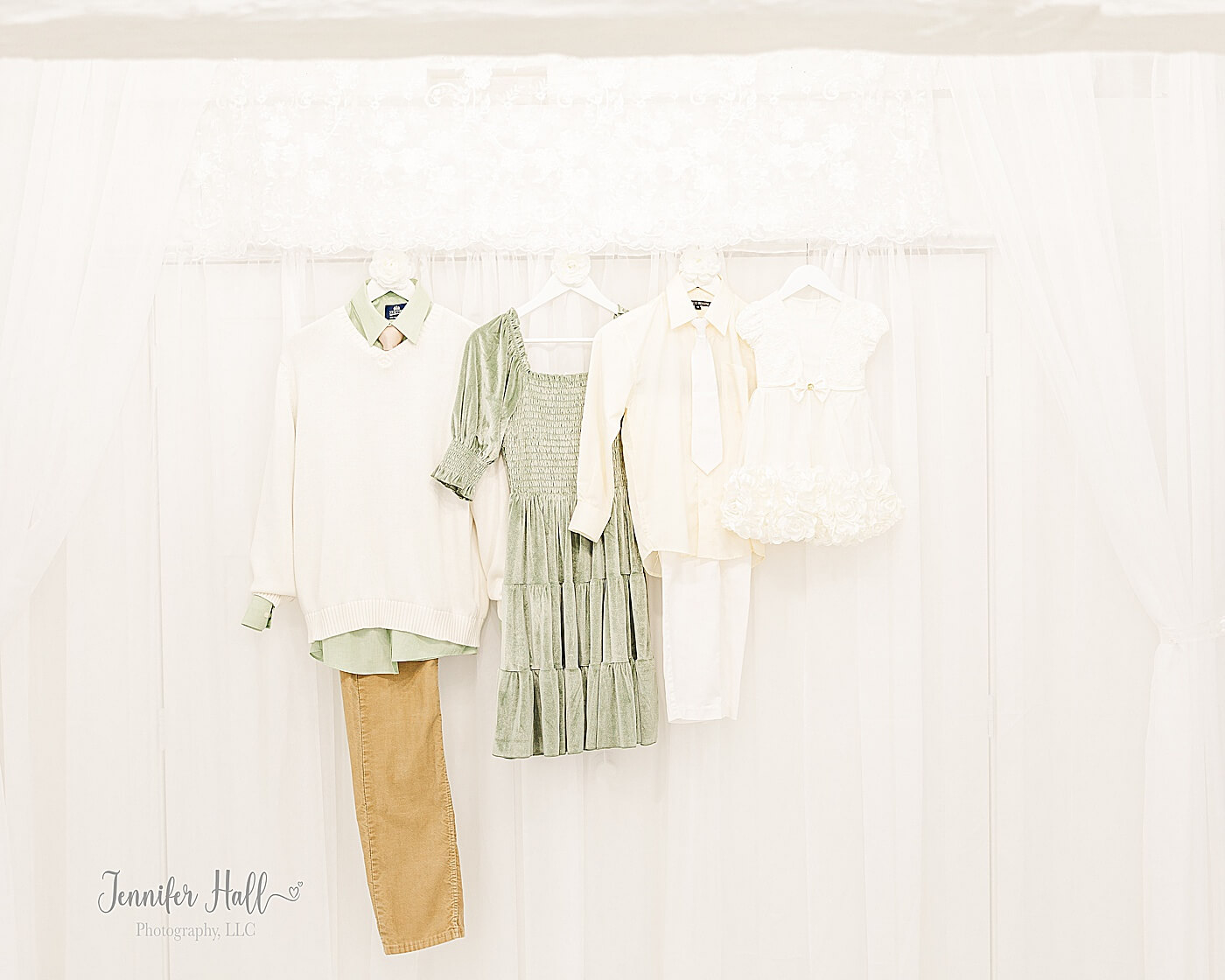 Dusty sage and tan family outfits hanging in a white studio to show how to coordinate outfits for a family photo session.