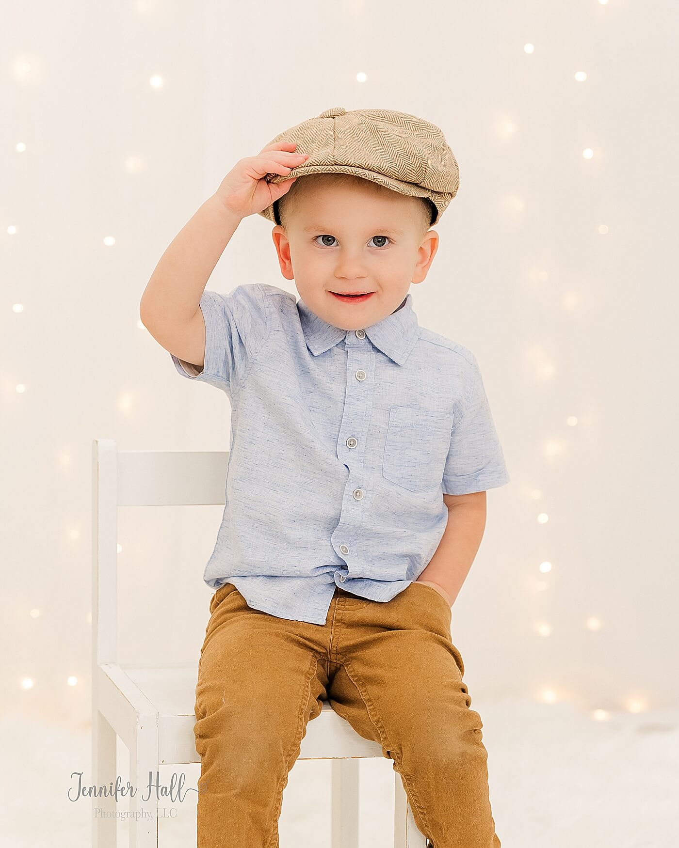 Little boy with a powder blue solid, collared shirt, a newsboy cap, and mustard pants in a white studio for a family portrait session outfit idea.