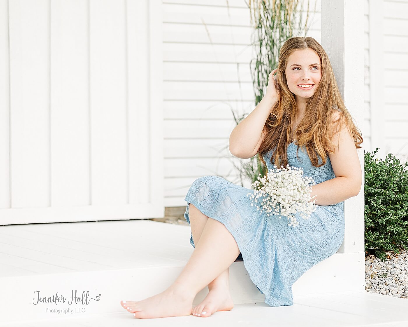 Senior girl with a powder blue dress sitting on an "Outside Grand Entrance" and holding white flowers, showing girl portrait outfit ideas.