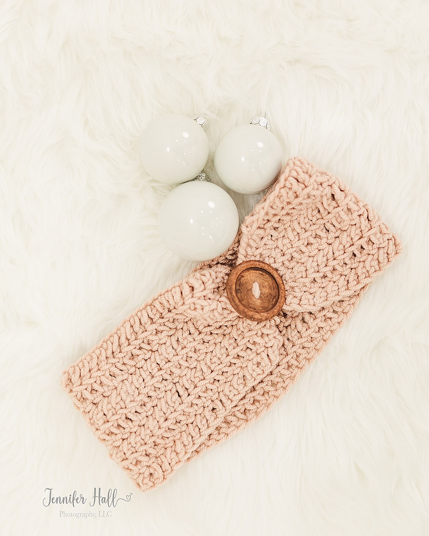 Champagne ear warmer with a wooden button laying on a white blanket in a photo studio.