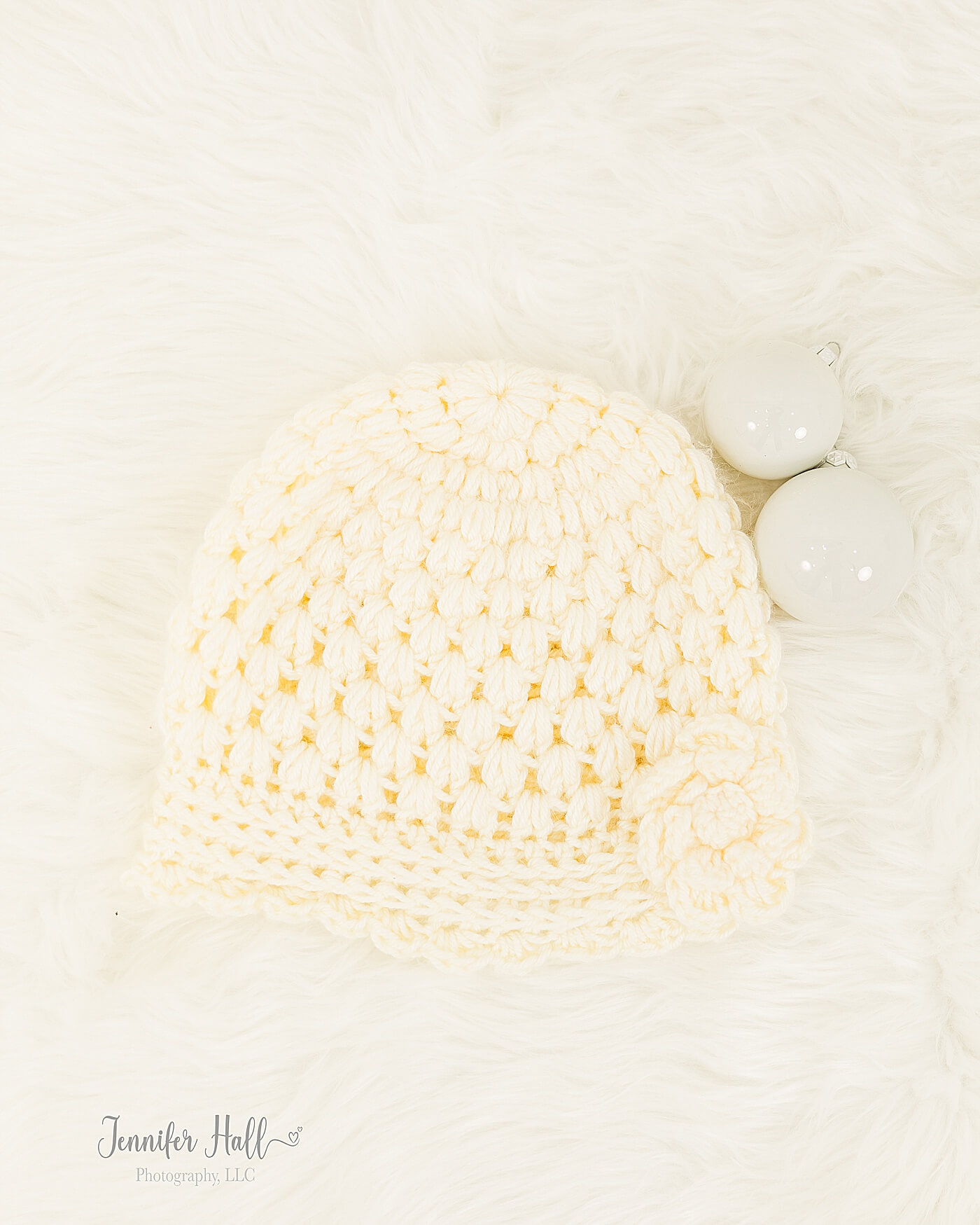 Cream, vintage hat with a flower laying on a white blanket by white Christmas bulbs.