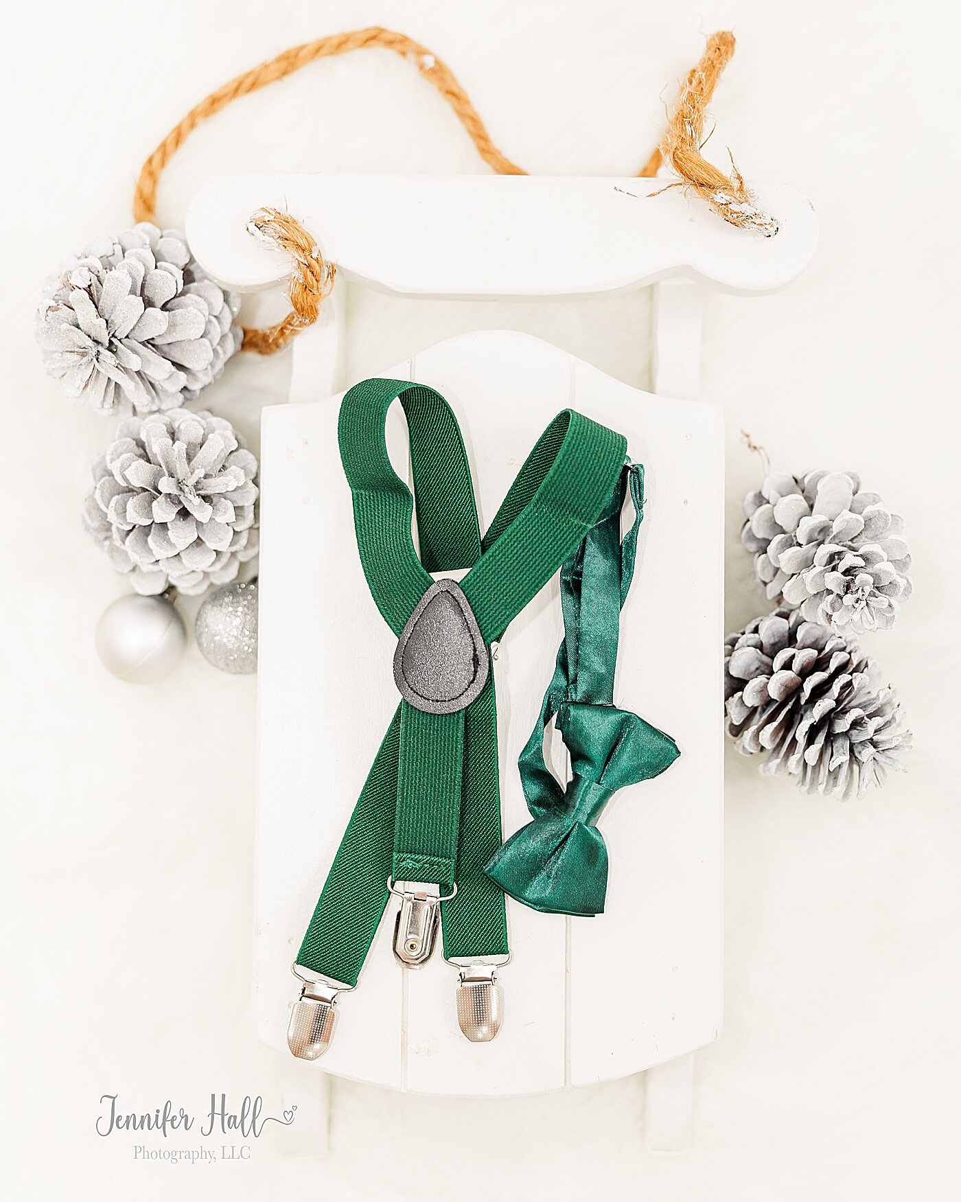 Emerald boy tie and suspenders laying on a small, white sleigh for Christmas family photo accessories.