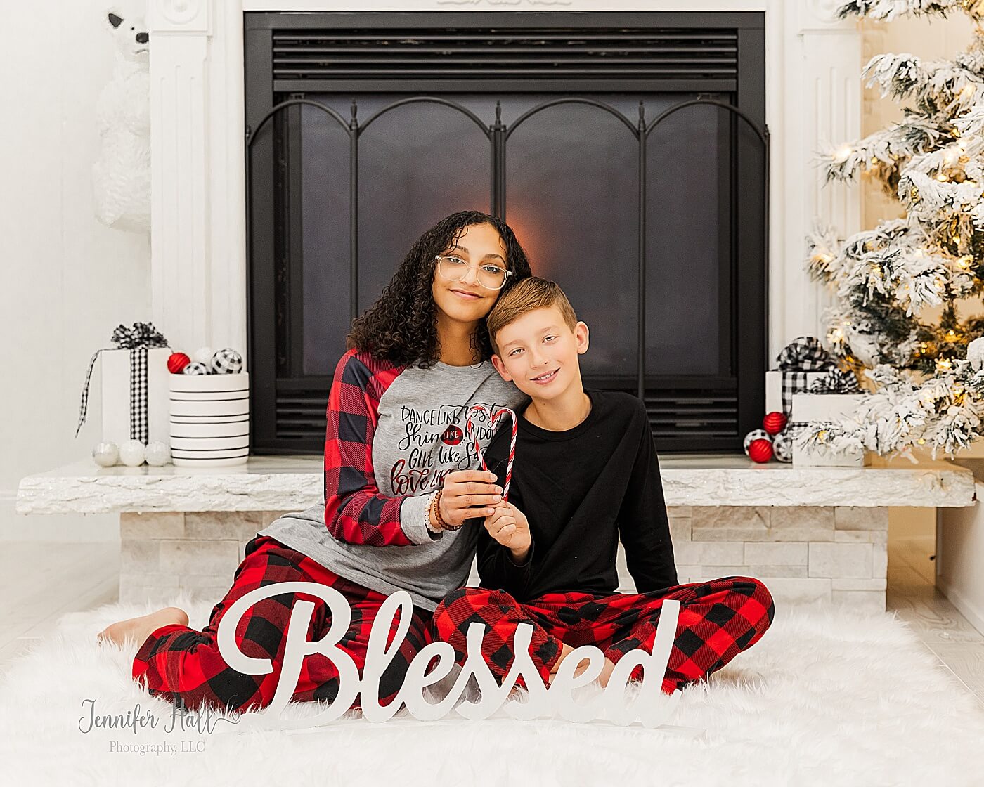 Brother and sister sitting by a fireplace with the word "Blessed" for Christmas family photos in-studio.