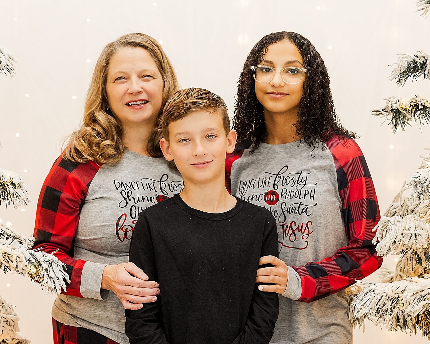 The family is standing together indoors by white, snowy Christmas trees.