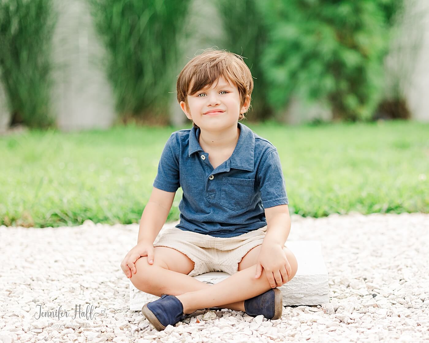 Little boy with a navy collared shirt smiling and sitting outdoors on wood.