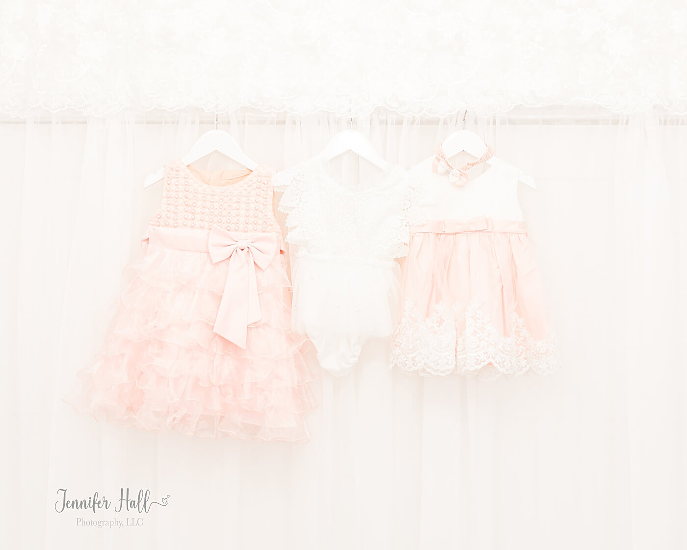 Little girls’ pink and white dresses and a white onesie hanging up indoors.