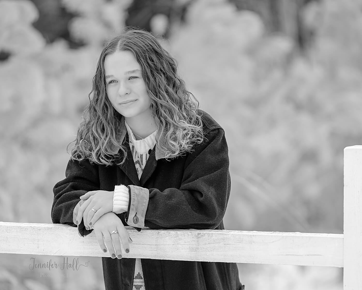 Girl leaning against a white, split-rail fence for winter senior photography in North East, PA.