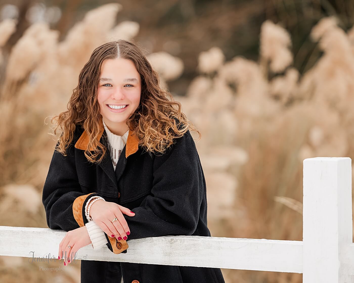 Girl standing by a white, split-rail fence for winter senior photos near Erie, PA.
