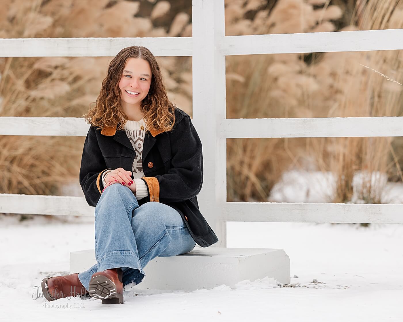 Girl sitting on a white wooden box and smiling for winter senior pictures.