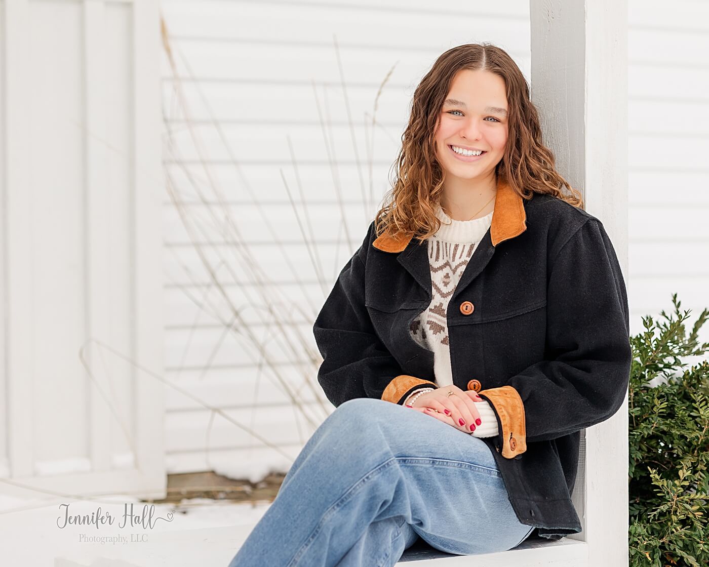 Senior girl sitting at the outside grand entrance and smiling during winter.
